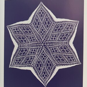 May include: A white, star-shaped doily with intricate lace detailing. The doily is set against a dark blue background, creating a striking contrast. The lace pattern features a combination of openwork and solid areas, forming a delicate and elegant design. This item is perfect for home decor.