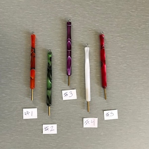 May include: Five cylindrical tools with metallic tips and small loops at the top, labeled #1 through #5. The tools feature marbled patterns in orange, green, purple, white, and red. Each tool has a slender, straight body and a short, gold-colored metal tip.