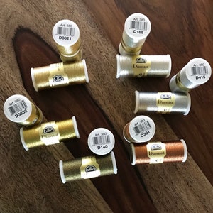 May include: Assortment of DMC Diamant embroidery floss spools in gold, silver, and copper colors. The spools have labels with the text "Art. 380" and a corresponding number.