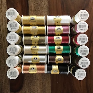 May include: A collection of 12 spools of DMC Diamant embroidery thread in various metallic colors, including gold, silver, red, green, and brown. Each spool is labeled with the DMC Art. 380 number and a unique code.