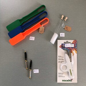 May include: A set of embroidery tools including three plastic needle threaders, two wooden needle threaders, a pair of single-ring thread scissors, and a white foam brush.