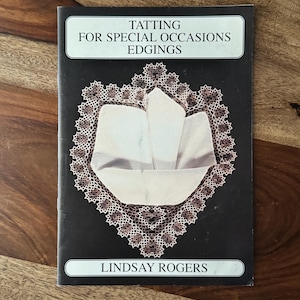 May include: A book titled "Tatting for Special Occasions Edgings" by Lindsay Rogers. The cover features a black background with a white and brown lace design surrounding a folded white cloth.