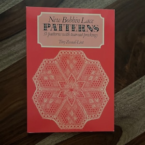 May include: A red book titled "New Bobbin Lace Patterns" with the subtitle "35 patterns with tear-out prickings" and the author's name "Tiny Zwaal-Lint". The cover features a white bobbin lace doily.