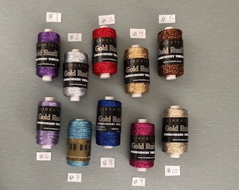 May include: Ten spools of metallic embroidery thread in various colors, including purple, silver, red, gold, brown, blue, teal, pink, and gold. Each spool is labeled "Gold Rush Embroidery Thread" with the company's website address.