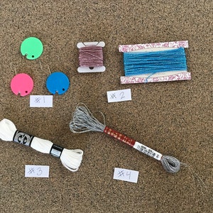 May include: Assortment of embroidery floss spools in various colors, including white, blue, silver, and pink. The spools are labeled with numbers 1 through 4.