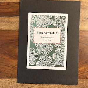May include: A black book with the title "Lace Crystals 2" by Dana Mihulkova and Irena Ring. The cover features a design of white lace snowflakes on a green background.