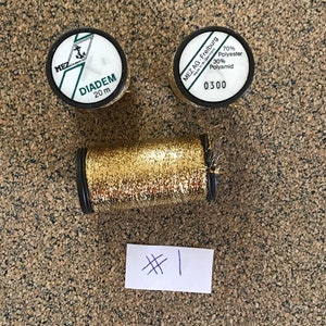 May include: Two spools of gold metallic thread, one labeled "DIADEM 20 m" and the other "MEZ AG. Freiburg Made in W-Germany 70% Polyester 30% Polyamid 0300".