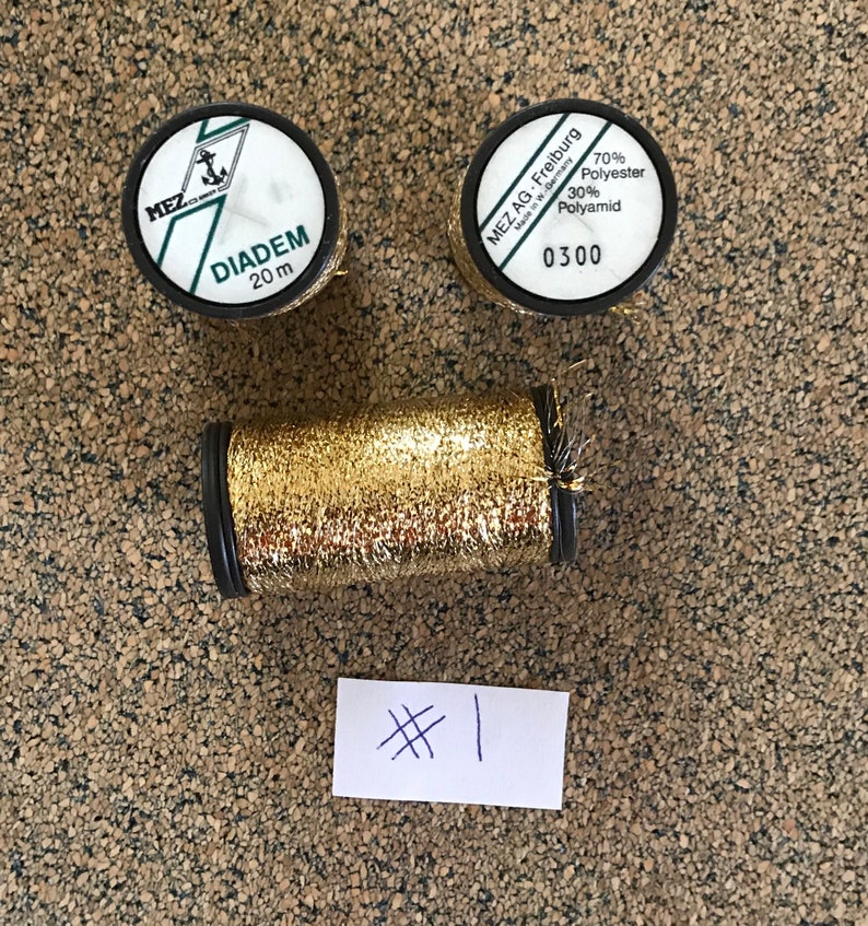 May include: Two spools of gold metallic thread, one labeled "DIADEM 20 m" and the other "MEZ AG. Freiburg Made in W-Germany 70% Polyester 30% Polyamid 0300".