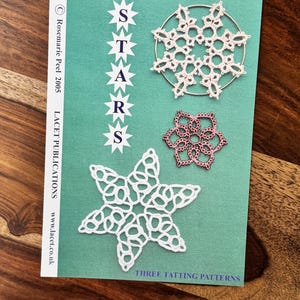 May include: A teal card with the word "STARS" in white star-shaped text. The card features three tatting patterns: a white snowflake, a pink flower, and a white star. The text "THREE TATTING PATTERNS" is at the bottom.