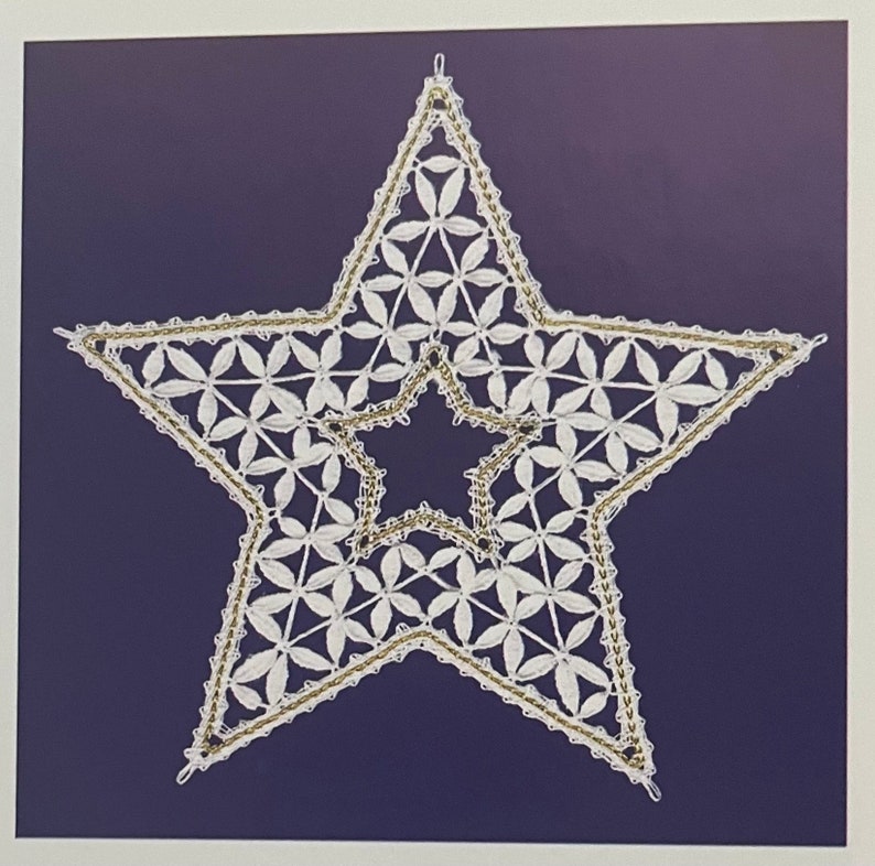 May include: A white, star-shaped, handmade lace ornament with a gold-colored border and a dark blue background. The star is filled with a floral pattern and has a smaller star shape in the center. The ornament is likely for holiday or home decor.