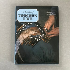 May include: A book titled "The Technique of Torchon Lace" by Pamela Nottingham. The cover features a close-up of a person's hands working on a piece of lace with bobbins.
