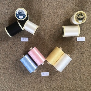 May include: Three spools of white thread, one spool of black thread, one spool of light blue thread, and one spool of pink thread. The spools are labeled with the DMC brand name.