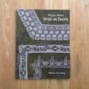 May include: A book cover with a green background and white lace patterns. The title is "SPITZEN UND EINSÄTZE" by Brigitte Bellon. The book is published by Barbara Fay Verlag.