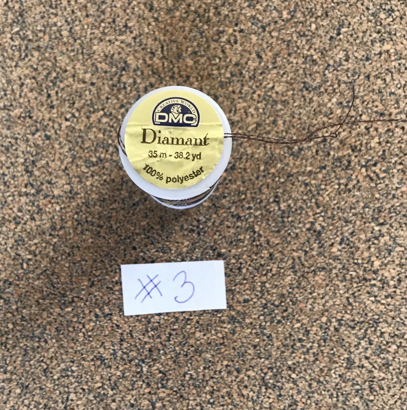 May include: A spool of brown Diamant embroidery thread by DMC. The label reads "Diamant 35 m - 38.2 yd 100% polyester". The spool is labeled with the number "3".