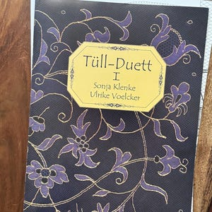 May include: A book cover with a gold and purple floral design. The title is "Tüll-Duett I" with the authors "Sonja Klenke" and "Ulrike Voelcker" listed below.