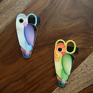 May include: Two colorful bird-shaped scissor holders. One is blue, purple, and white with blue polka dots. The other is green, yellow, and orange with yellow polka dots.