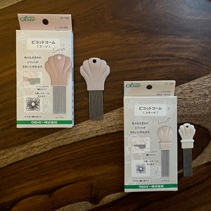 May include: Two packages of Clover brand crochet tools. The packages are pink and white with Japanese text. The tools are called "Picot Combs" and come in two sizes: Large and Small. The tools are shaped like seashells and have a row of metal teeth.