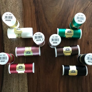 May include: Assortment of DMC Diamant embroidery floss spools in various colors, including red, black, brown, white, and green. Each spool has a label with the text "Art. 380" and a unique code, such as "D316" or "D699".