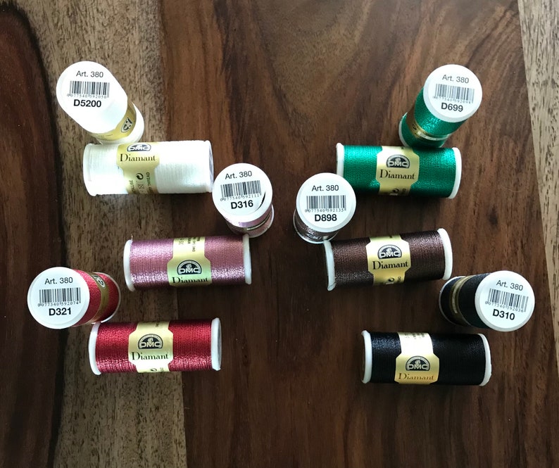 May include: Assortment of DMC Diamant embroidery floss spools in various colors, including red, black, brown, white, and green. Each spool has a label with the text "Art. 380" and a unique code, such as "D316" or "D699".