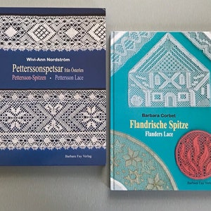 May include: Two books about lacemaking. The book on the left is blue with white lace patterns and the title "Petterssonspetsar från Österlen Pettersson-Spitzen Pettersson Lace". The book on the right is turquoise with white lace patterns and the title "Flandrische Spitze Flanders Lace". Both books have the publisher "Barbara Fay Verlag" printed on the bottom.