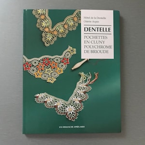 May include: A book titled "DENTELLE" with the text "POCHETTES EN CLUNY POLYCHROME DE BRIOUDE" on a green cover. The cover features colorful lace designs and a wooden bobbin. The book is by Odette Arpin.
