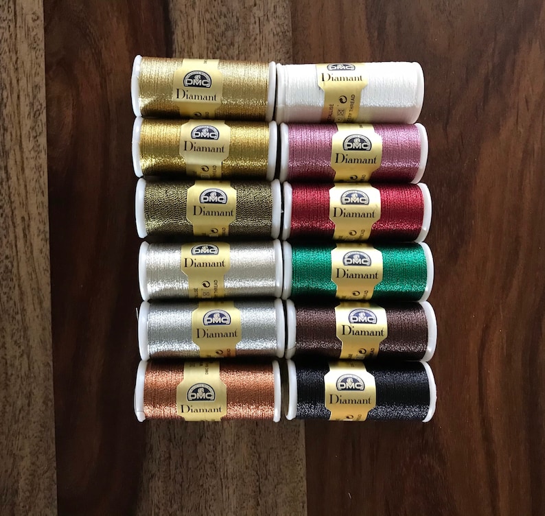 May include: A collection of 12 spools of DMC Diamant embroidery thread in various metallic colors, including gold, silver, copper, and red.