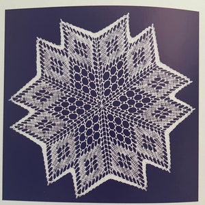 May include: A white, star-shaped doily with a detailed lace pattern. The doily features a central circular design surrounded by a series of pointed edges. The intricate openwork creates a delicate and elegant appearance.