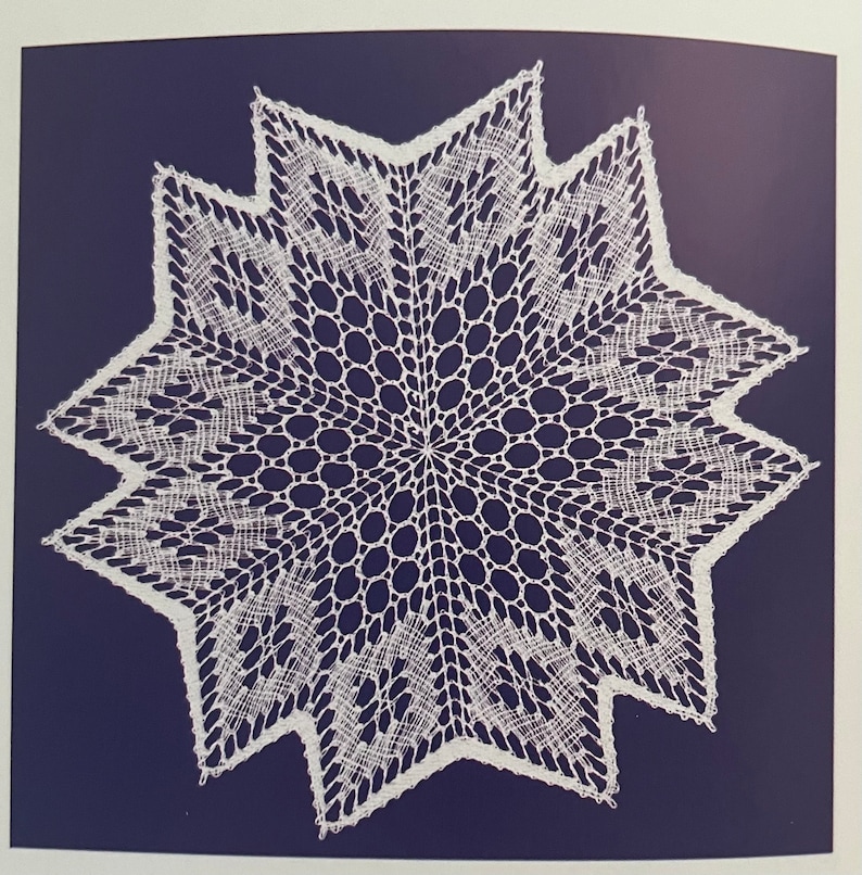 May include: A white, star-shaped doily with a detailed lace pattern. The doily features a central circular design surrounded by a series of pointed edges. The intricate openwork creates a delicate and elegant appearance.