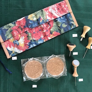 May include: A floral fabric roll-up case with a blue ribbon, two cork coasters in clear plastic packaging, and four wooden push pins with black tops.