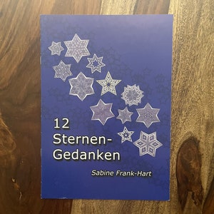 May include: A book cover with a dark blue background featuring white star illustrations of varying designs. The title "12 Sternen-Gedanken" is displayed in white, along with the author's name, Sabine Frank-Hart, in a smaller font.