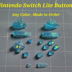 May include: A collection of transparent blue Nintendo Switch Lite buttons. The image includes various button shapes, including directional pads, face buttons, and shoulder buttons. Text at the top reads "Nintendo Switch Lite Buttons" and "Any Color, Made to Order".