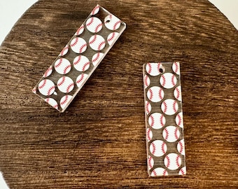May include: Two rectangular baseball-themed acrylic charms. Each charm features a pattern of white baseballs with red stitching against a clear background. The charms have a small hole at the top for hanging.