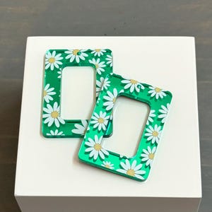 May include: Two green acrylic frames with a white daisy pattern. The frames are rectangular with rounded corners and have a cutout in the center.