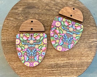 May include: Two-part earrings with a floral design. The main body of the earrings is a shield shape with a colorful floral pattern in pink, yellow, blue, and green. The top piece is a half-circle of wood with two holes.
