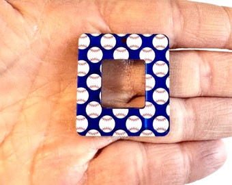 May include: A square-shaped acrylic charm with a blue background and a white outline. The charm is decorated with a repeating pattern of white baseballs with red stitching. The charm has a square cutout in the center.