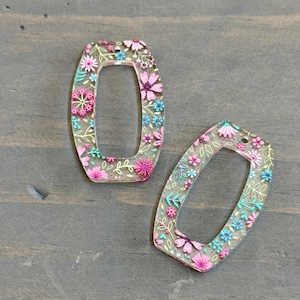 May include: Two clear acrylic charms with a floral design. The charms are shaped like a rectangle with rounded corners and have a hole at the top for hanging.
