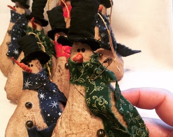 May include: A group of handmade snowman ornaments with different colored scarves and hats. The ornaments are made of burlap and have a rustic look.