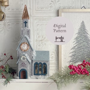 Könnte beinhalten: Ein Weihnachtskirchenornament aus Filz mit einem weißen Turm, blauen Fenstern und einem Zifferblatt. Das Ornament steht auf einem weißen Regal mit einem verschneiten Hintergrund und einem Weihnachtsbaum im Hintergrund. Der Text "Digitales Muster" ist in einem Kreis mit einem Nähmaschinen-Symbol sichtbar.