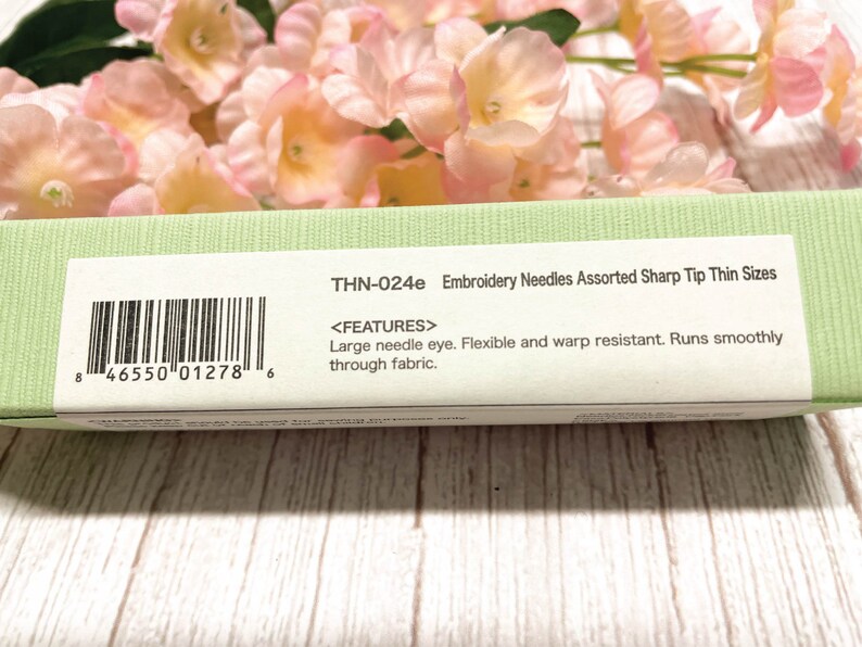 Puede incluir: Un paquete verde y blanco de agujas de bordar con el texto "THN-024e Embroidery Needles Assorted Sharp Tip Thin Sizes" y un c&oacute;digo de barras. El paquete tambi&eacute;n incluye el texto "<FEATURES> Large needle eye. Flexible and warp resistant. Runs smoothly through fabric."