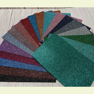 Op de afbeelding: Een waaier van 18 verschillende kleuren glitterpapier. Het papier is in een halve cirkel gerangschikt met het groene glitterpapier onderaan.