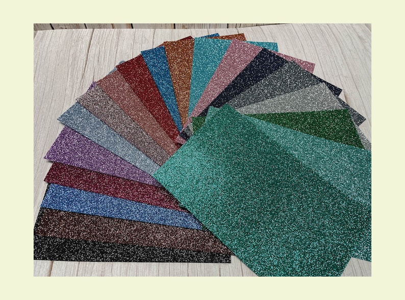 Op de afbeelding: Een waaier van 18 verschillende kleuren glitterpapier. Het papier is in een halve cirkel gerangschikt met het groene glitterpapier onderaan.