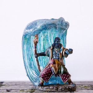 Könnte beinhalten: Eine blau und grün bemalte Miniaturfigur eines humanoiden Wesens mit einem Stab, das vor einer blau und grünen Welle steht. Die Figur ist mit goldenen Akzenten bemalt und steht auf einem grauen Sockel.