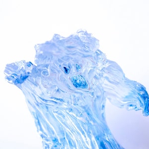 Puede incluir: Una escultura de hielo azul translúcido de una criatura con un diseño arremolinado y fluido. La escultura está de pie sobre una superficie de piedra gris.