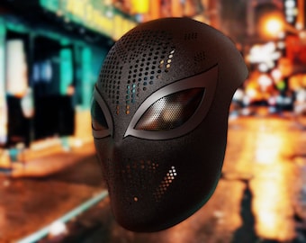 May include: A black mask with a textured surface and a perforated design. The eye openings are outlined with a metallic silver trim. The mask has a futuristic, superhero-inspired aesthetic.