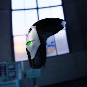 May include: A black and white mask with a green eye. The mask is made of plastic and has a smooth surface.