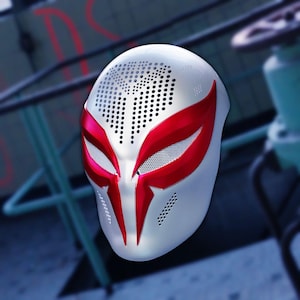 Könnte beinhalten: Eine weiße Vollmaske mit perforierter Textur im Stirn- und Wangenbereich. Die Maske ist mit scharfen, metallisch roten, augenförmigen Markierungen akzentuiert, die sich bis zum Nasenrücken erstrecken und ein markantes grafisches Design bilden.