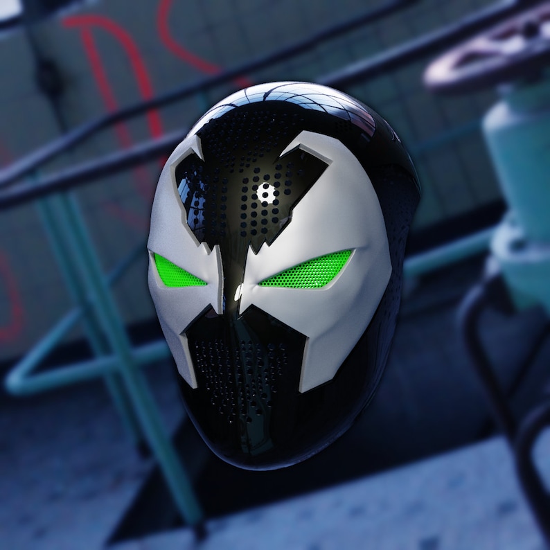 May include: A black and white mask with green eyes. The mask has a textured surface and a pointed chin.
