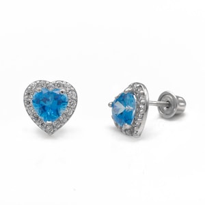 May include: A pair of silver heart-shaped earrings with a blue topaz gemstone in the center of each heart. The hearts are surrounded by a halo of smaller clear gemstones.
