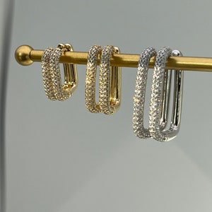 Può includere: Tre paia di orecchini a cerchio con una doppia fila di pietre di zircone cubico. Gli orecchini sono in oro, argento e oro rosa.