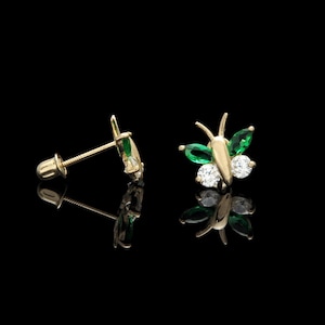 Op de afbeelding: Een paar gouden vlinder oorringen met groene en witte edelstenen. De oorringen zijn op een zwarte achtergrond.